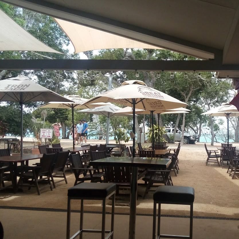 Shaded outdoor beachfront dining tables with umbrellas at a Cape Gloucester resort near Hideaway Bay accommodation.