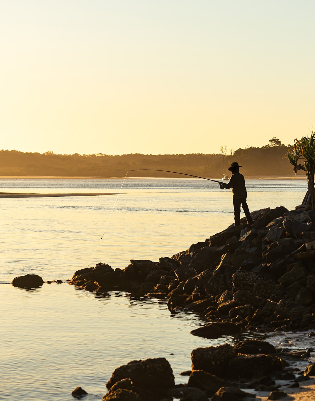 A fisherman casting a line from the rocky shore at sunset in Bowen near Hideaway Bay.