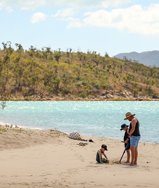 A parent and child wading in the calm, shallow waters at Dingo Beach near Hideaway Bay accommodation.