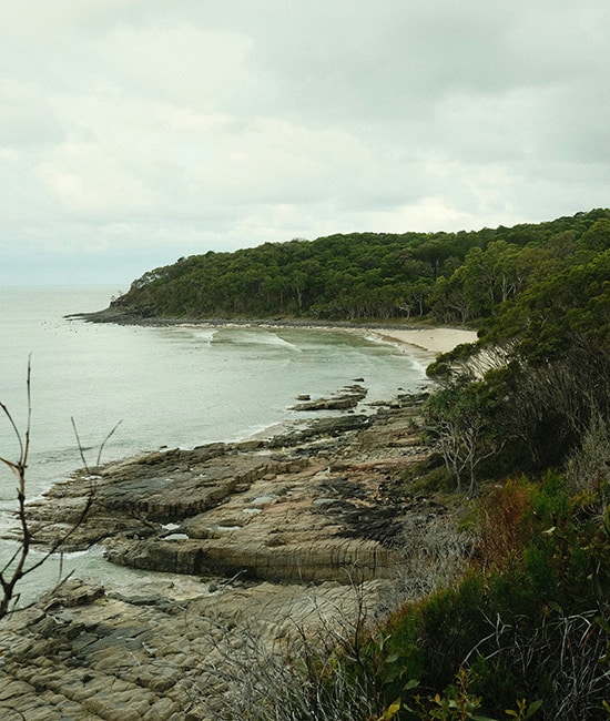 Secluded sandy cove and lush green headland at Hideaway Bay Beach in the Whitsundays.